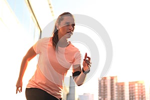 Young attractive sporty fitness woman running while exercising outdoors at sunset or sunrise in city.