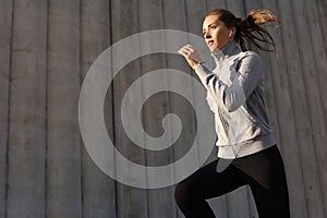 Young attractive sporty fitness woman running while exercising outdoors at sunset or sunrise in city