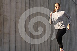 Young attractive sporty fitness woman running while exercising outdoors at sunset or sunrise in city