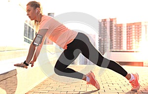 Young attractive sporty girl doing push ups, outdoors at sunset or sunrise in city.