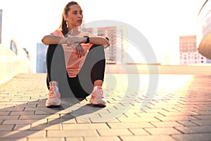Young attractive sporty girl resting on the street with mobile phone and music, outdoor at sunset or sunrise in city.