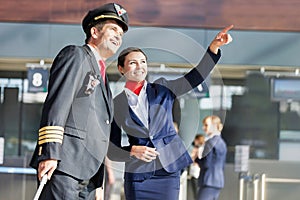 Young attractive stewardess pointing aircraft with the pilot in airport