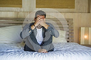 Young attractive stressed and depressed man sitting on bed worried and frustrated suffering depression crisis covering face with