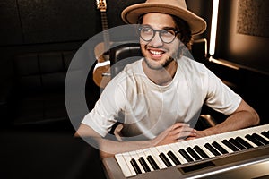 Young attractive stylish musician happily working in modern recording studio. Smiling man composing song in studio