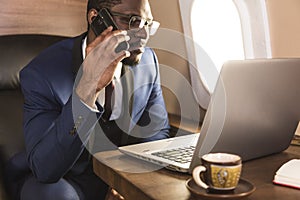 Young attractive and successful African American businessman with glassies talking on the phone and working while