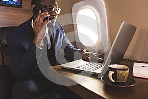 Young attractive and successful African American businessman with glassies talking on the phone and working while