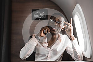 Young attractive and successful African American businessman with glassies talking on the phone and working while