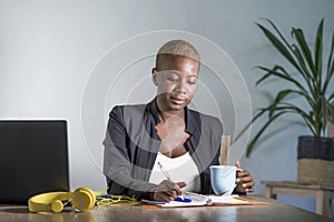 Young attractive and successful black afro american woman in business jacket working serious at office laptop taking notes writing