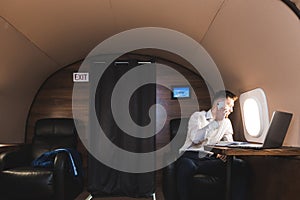 Young attractive and successful businessman talking on the phone and working while sitting in the chair of his private