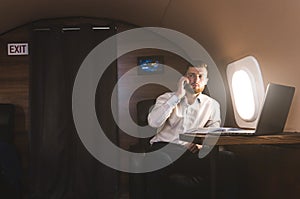 Young attractive and successful businessman talking on the phone and working while sitting in the chair of his private