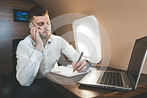 Young attractive and successful businessman talking on the phone and working while sitting in the chair of his private