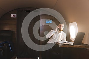 Young attractive and successful businessman talking on the phone and working while sitting in the chair of his private