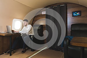 Young attractive and successful businessman working while sitting in the chair of his private business plane