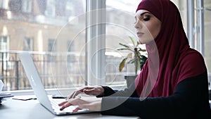 Young attractive supposedly muslim girl typing something on her laptop. Indoors footage