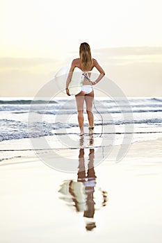 Young attractive surfer girl with board looking out at the waves