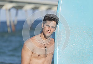 Young attractive surfer holding his surfboard at the beach