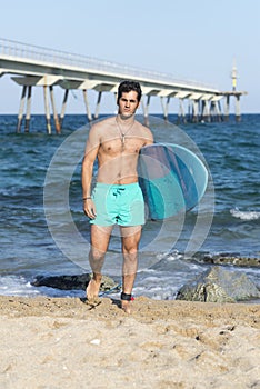 Young attractive surfer holding his surfboard at the beach