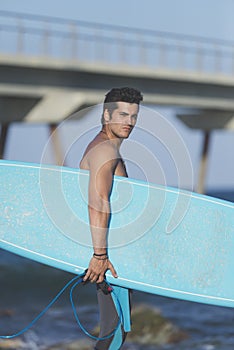 Young attractive surfer holding his surfboard at the beach