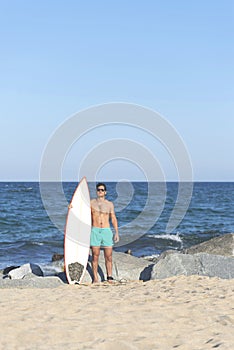 Young attractive surfer holding his surfboard at the beach