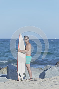 Young attractive surfer holding his surfboard at the beach