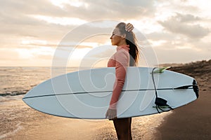 Young attractive surfer woman with white board at sunset on the ocean. Bali Indonesia.