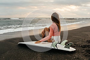 Young attractive surfer woman with white board at sunset on the ocean. Bali Indonesia.