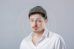 Young attractive surprised brunette man in white shirt on gray