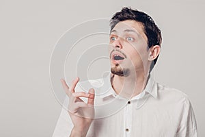 Young attractive surprised brunette man in white shirt on gray b