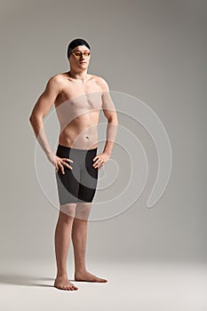 Young attractive swimmer in excellent physical shape in purple swimming shorts, on a gray background, copy space