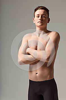 Young attractive swimmer in excellent physical shape in purple swimming shorts, on a gray background, copy space