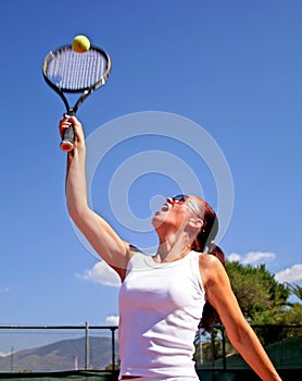 Young attractive tanned healthy woman playing tennis in midday sun with blue sky