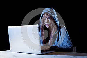 Young attractive teen woman wearing hood on hacking laptop computer cybercrime cyber crime concept