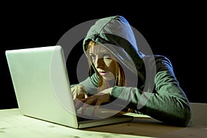 Young attractive teen woman wearing hood on hacking laptop computer cybercrime cyber crime concept