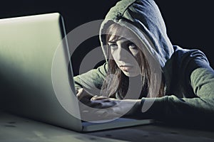 Young attractive teen woman wearing hood on hacking laptop computer cybercrime cyber crime concept