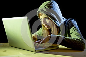 Young attractive teen woman wearing hood on hacking laptop computer cybercrime cyber crime concept photo