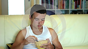 Young attractive teenager boy eat corn flakes while watching television on sofa