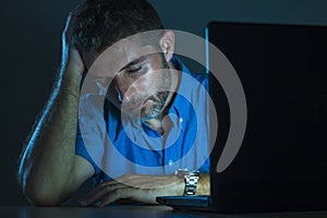 Young attractive and tired unshaven man working late night on laptop computer in the dark feeling frustrated and exhausted in