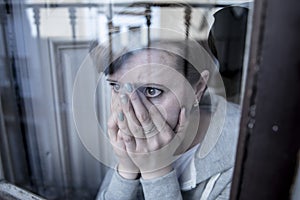 Young attractive unhappy depressed lonely woman looking sad looking through the window at home