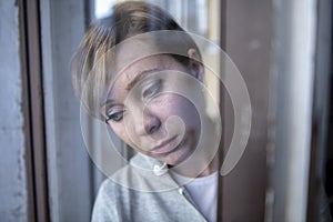 Young attractive unhappy depressed lonely woman looking worried and sad through the window at home