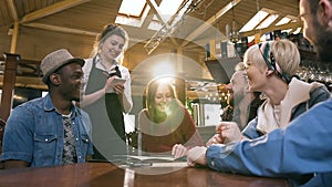 Young attractive waitress taking order from group of multi ethnic friends resting in the bar, pub.