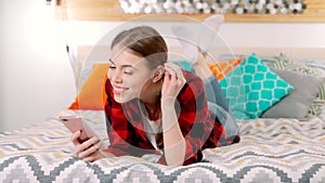 A young attractive white woman is lying on the bed smiling and holding a mobile phone in her hands and texting with her friend