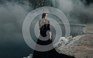 Young attractive Witch walking on the bridge in heavy black smoke.