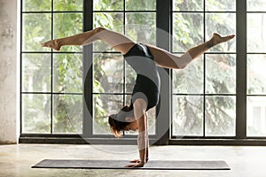 Young attractive woman in Adho Mukha Vrksasana pose, window back