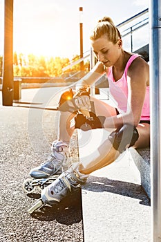 Young attractive woman adjusting safety gear while wearing rollerblades
