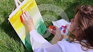 Young attractive woman artist paints on nature. Artist's palette with paints and brush Hobby. Creative artist painting