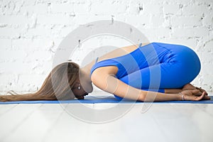 Young attractive woman in Balasana pose, white studio background