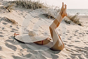 Young attractive woman in bikini with big straw hat posing at sandy beach