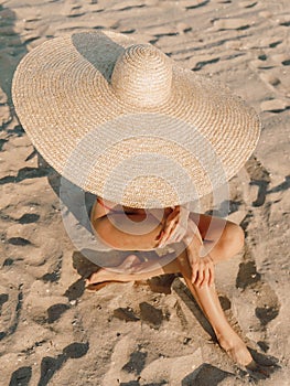 Young attractive woman in bikini with big straw hat posing at sandy beach photo