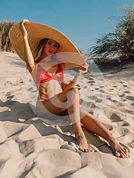 Young attractive woman in bikini with big straw hat posing at sandy beach