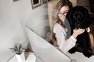 Young attractive woman with black cute dog speak with collegues by computer at home